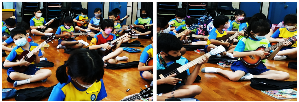Children wearing masks sit on a floor in a classroom playing ukuleles during a music lesson.